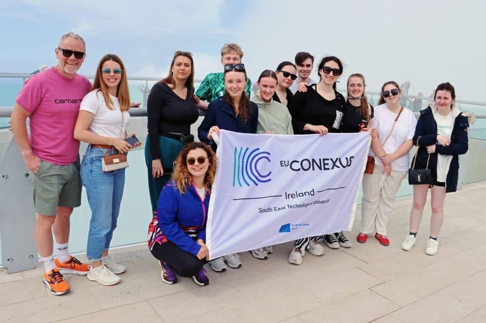Group of staff and students holding flag with water in the background