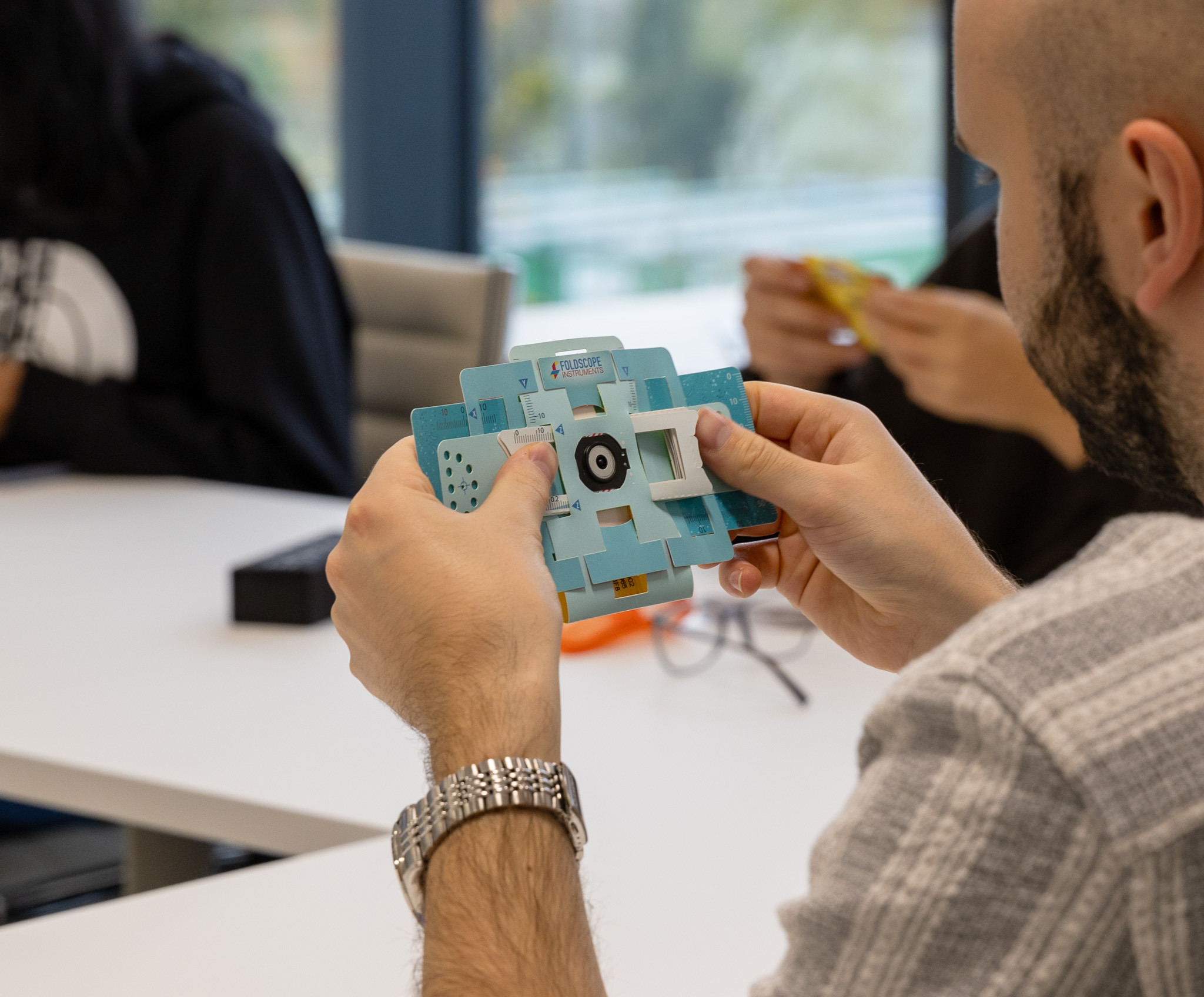 Student holding a Foldscope, a paper-based microscope developed through frugal innovation.