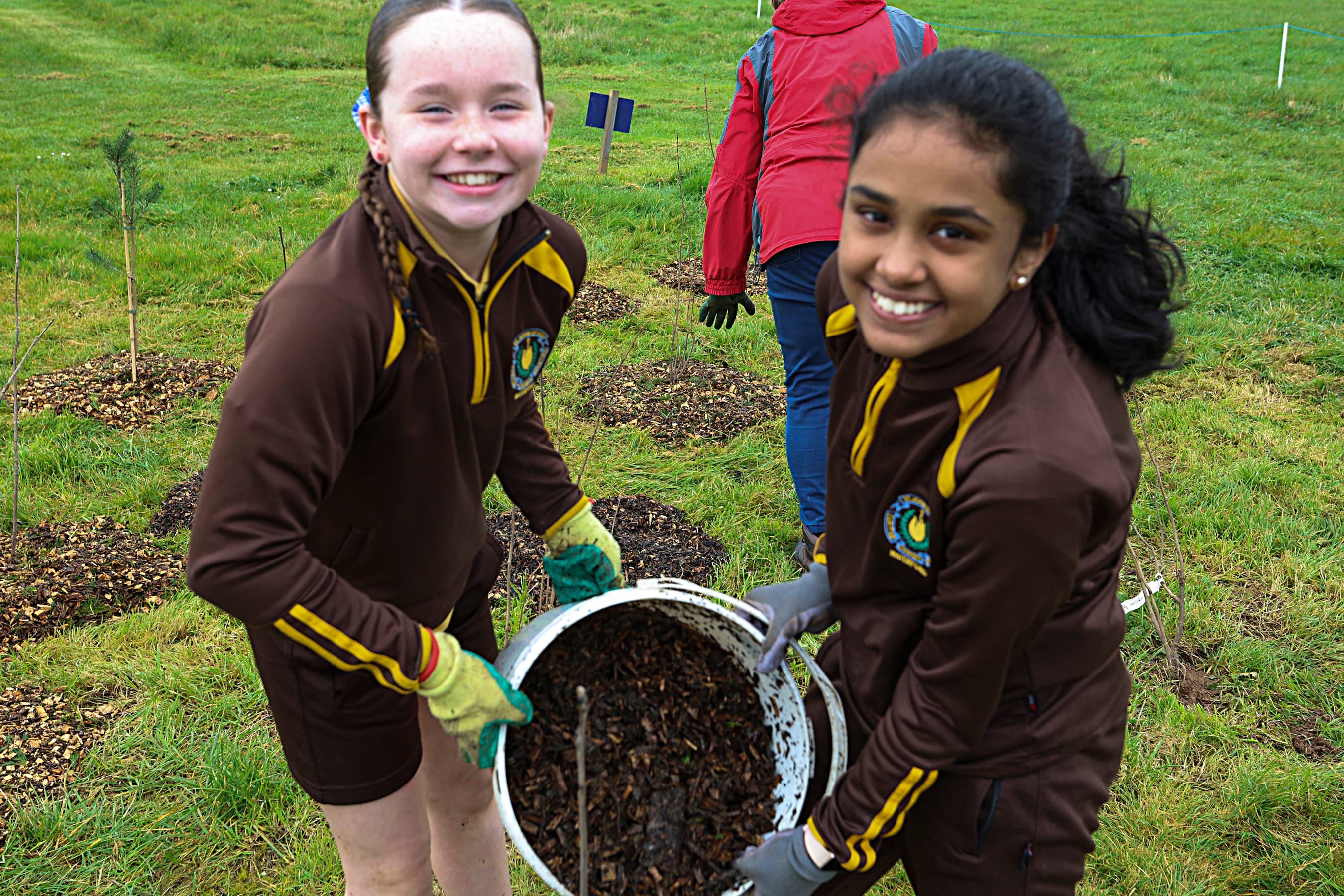 two students holding a bucket of soil