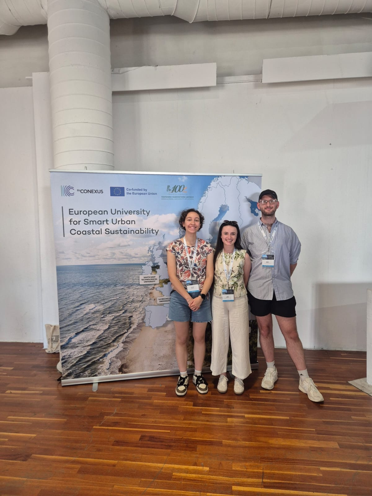 Three students standing in front of a pull-up with a map on it