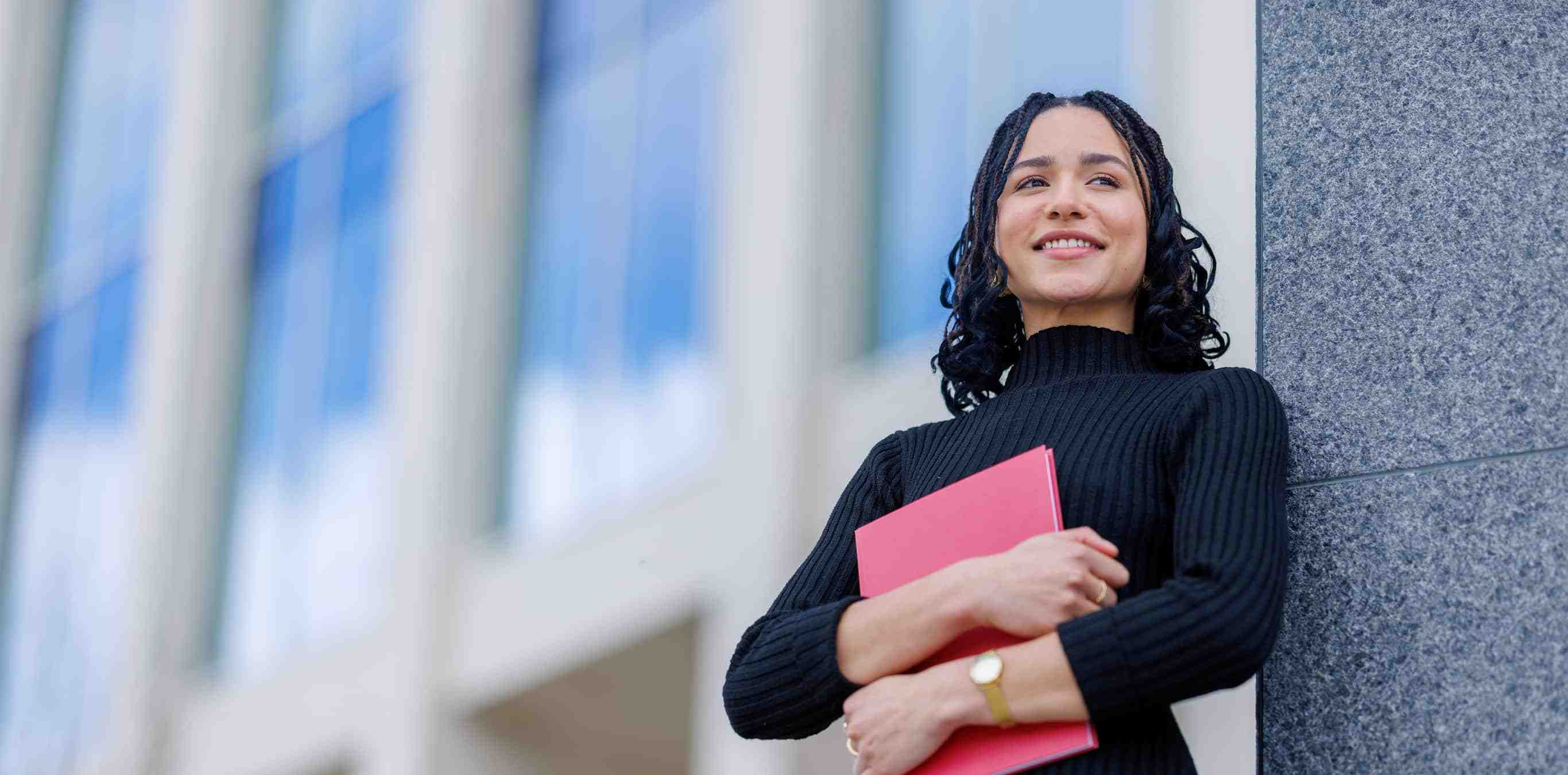 Girl standing against a building holding a red folder
