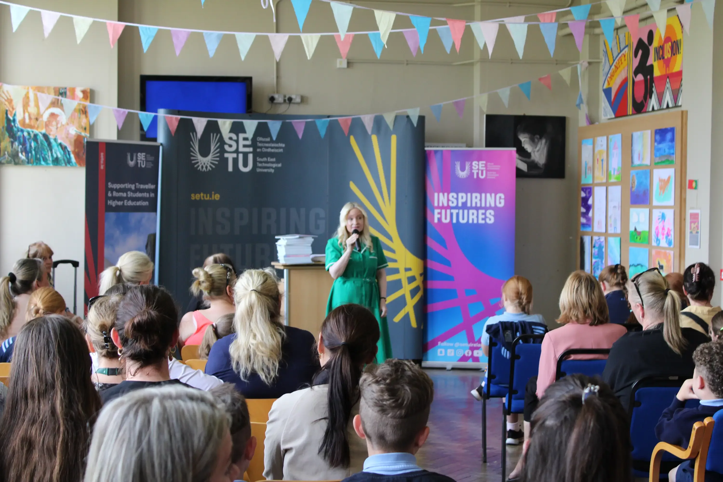 Woman speaking into microphone in front of a seated crowd